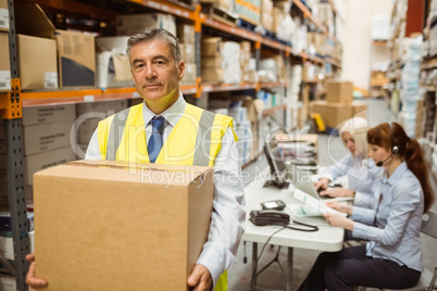 Warehouse manager smiling at camera carrying a box Warehouse manager smiling at camera carrying a box