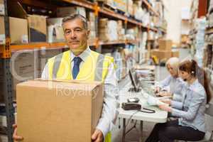 Warehouse manager smiling at camera carrying a box