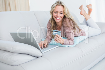 Smiling blonde lying on couch shopping online