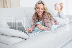 Smiling blonde lying on couch shopping online