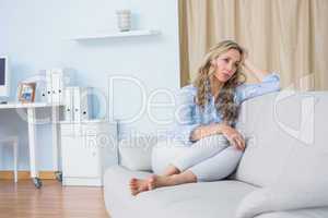 Blonde woman sitting on couch thinking