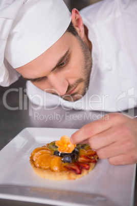 Focused baker putting flower on the pastry with fruit