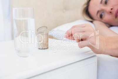 Pretty blonde lying bed taking pills on bedside table