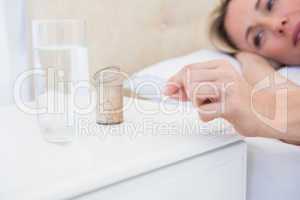 Pretty blonde lying bed taking pills on bedside table