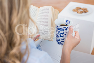 Blonde sitting on couch reading with cup of coffee