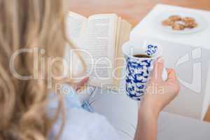 Blonde sitting on couch reading with cup of coffee