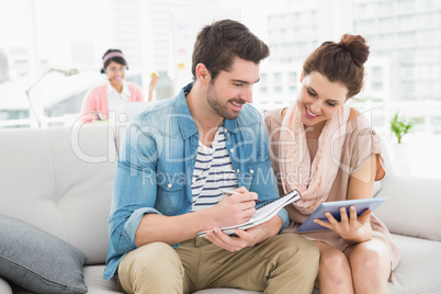 Smiling colleagues using tablet and taking notes on couch Smiling colleagues using tablet and taking notes on couch