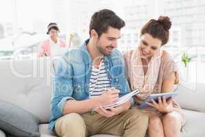 Smiling colleagues using tablet and taking notes on couch