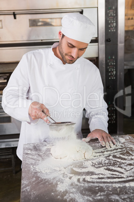 Focused baker sieving flour on the dough Focused baker sieving flour on the dough