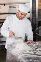 Focused baker sieving flour on the dough