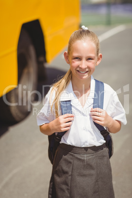 Cute pupil smiling at camera by the school bus