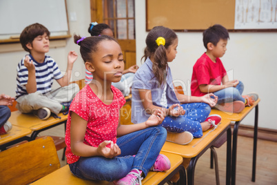 Pupils meditating in lotus position on desk in classroom