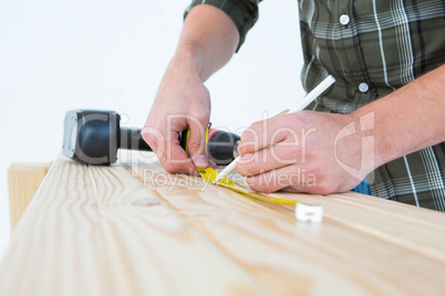 Carpenter using measure tape to mark on plank