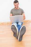 Casual man sitting on floor using laptop at home