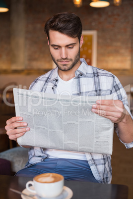 Young man having cup of coffee reading newspaper