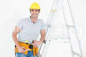 Worker holding tools while leaning on step ladder