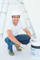 Happy man crouching while opening paint pot