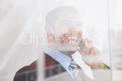 Smiling businessman out window at camera on the phone