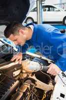 Mechanic examining under hood of car with torch