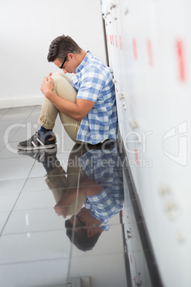 Thoughtful college student sitting against lockers