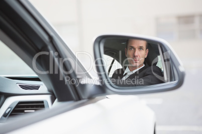 Businessman driving with his reflection in rear view mirror