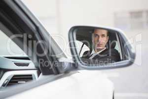 Businessman driving with his reflection in rear view mirror