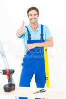 Carpenter leaning on spirit level while gesturing thumbs up