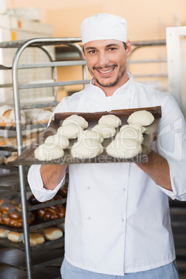 Smiling baker holding tray of raw dough