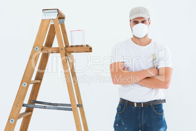 Man with paintbrush standing arms crossed by ladder