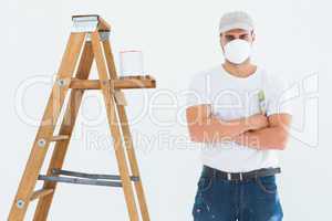 Man with paintbrush standing arms crossed by ladder