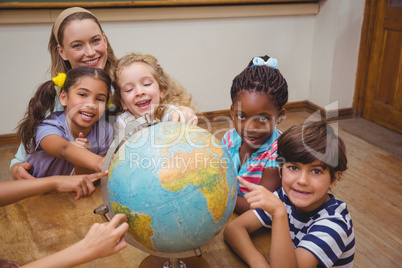 Cute pupils and teacher in classroom with globe