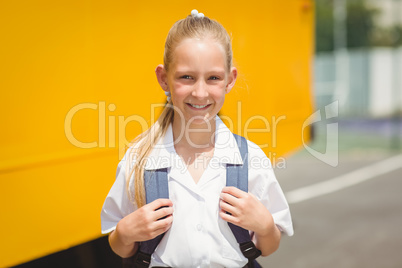 Cute pupil smiling at camera by the school bus