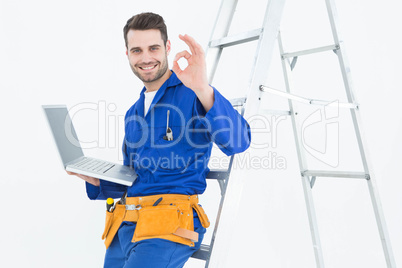 Construciton worker gesturing OK while leaning on ladder