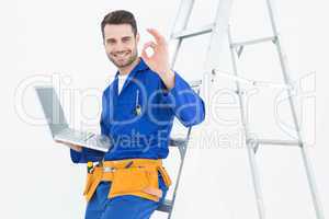 Construciton worker gesturing OK while leaning on ladder