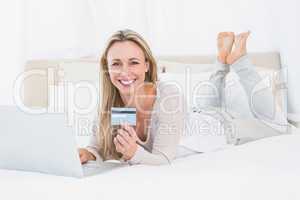 Smiling blonde shopping online on the bed