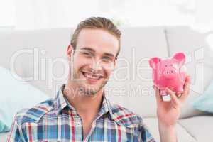 Smiling man showing pink piggy bank