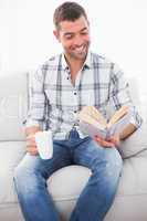A smiling man reading a book with a cup