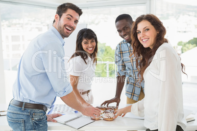 Smiling coworkers taking doughnut at desk