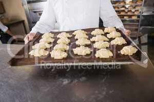 Close up of baker holding tray of raw dough