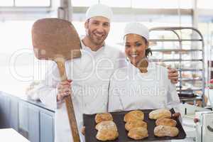 Team of bakers smiling at camera with trays of loaves