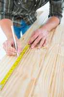 Carpenter marking with tape measure on wooden plank