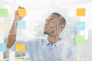 Thoughtful businessman writing on sticky notes on window