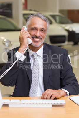 Smiling businessman using phone in front of computer