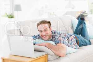 Happy man lying on sofa using laptop