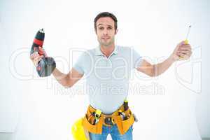 Confused technician holding screwdriver and drill machine
