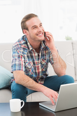 Smiling man on a phone with a laptop at home