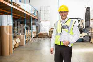 Warehouse manager wearing hard hat holding clipboard