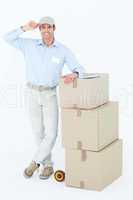 Happy delivery man leaning on stacked cardboard boxes