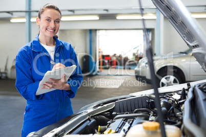 Mechanic smiling at the camera writing on clipboard Mechanic smiling at the camera writing on clipboard