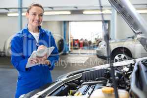 Mechanic smiling at the camera writing on clipboard